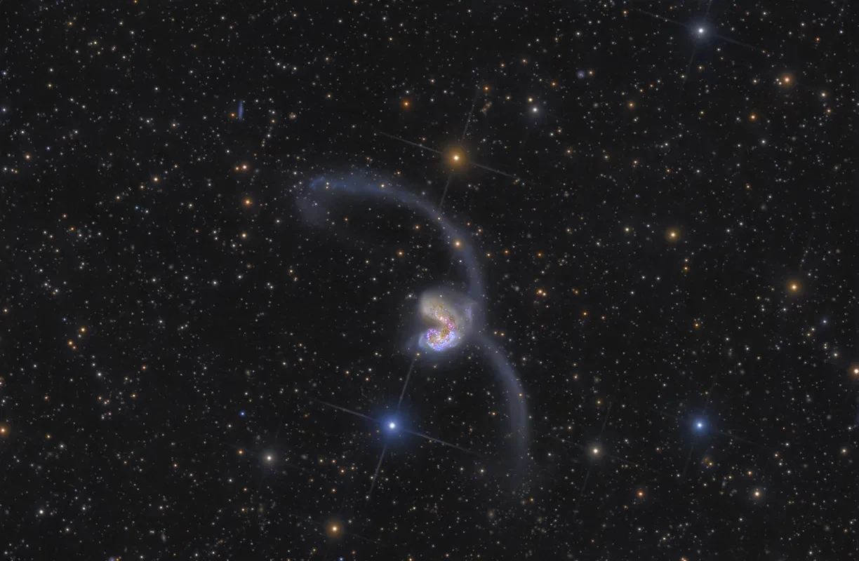 A swirling pair of colliding galexies in a black starry sky, with a bright centre.